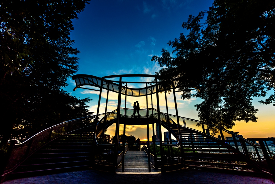 An engaged couple kiss on a bridge at sunset during their Battery Park Engagement Session.